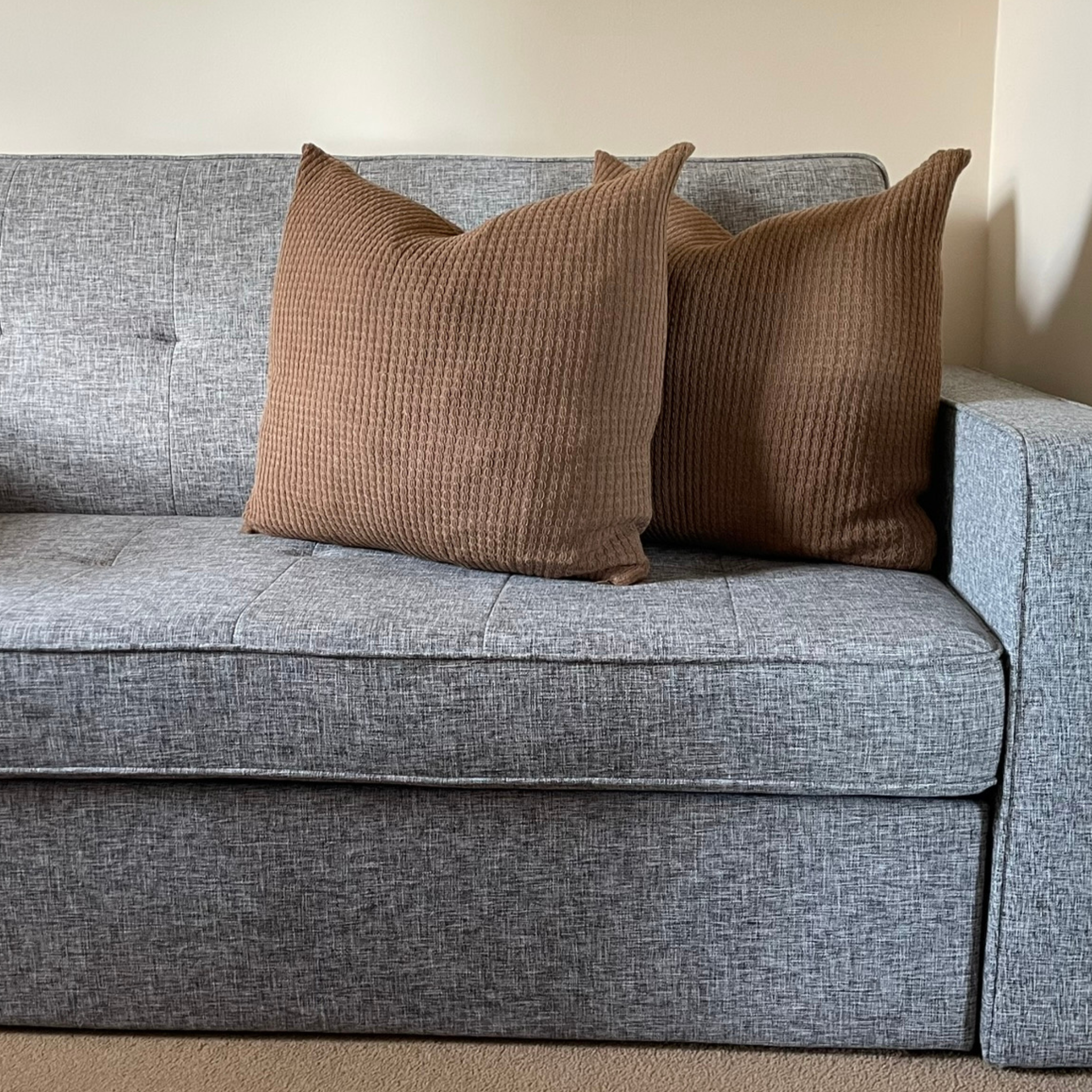Two cushions with brown alpaca pillow covers on a grey sofa