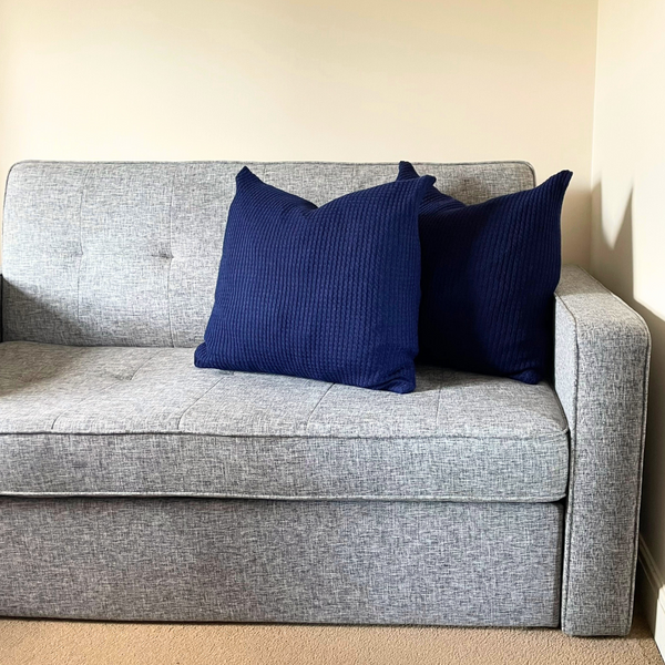 Two cushions with navy blue alpaca pillow covers on a grey sofa