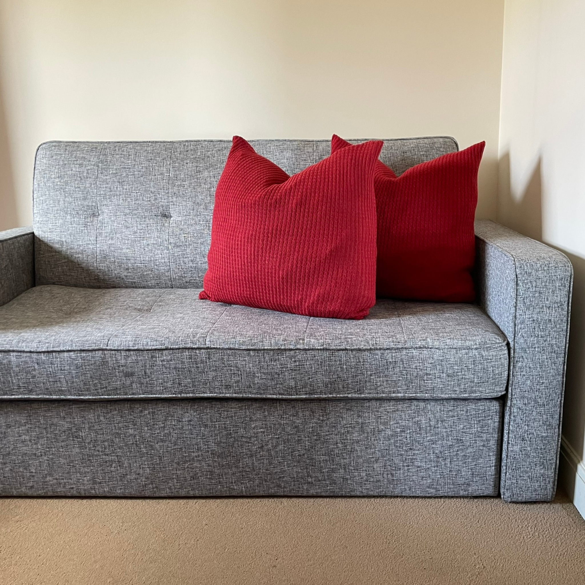 Two cushions with red alpaca pillow covers on a grey sofa