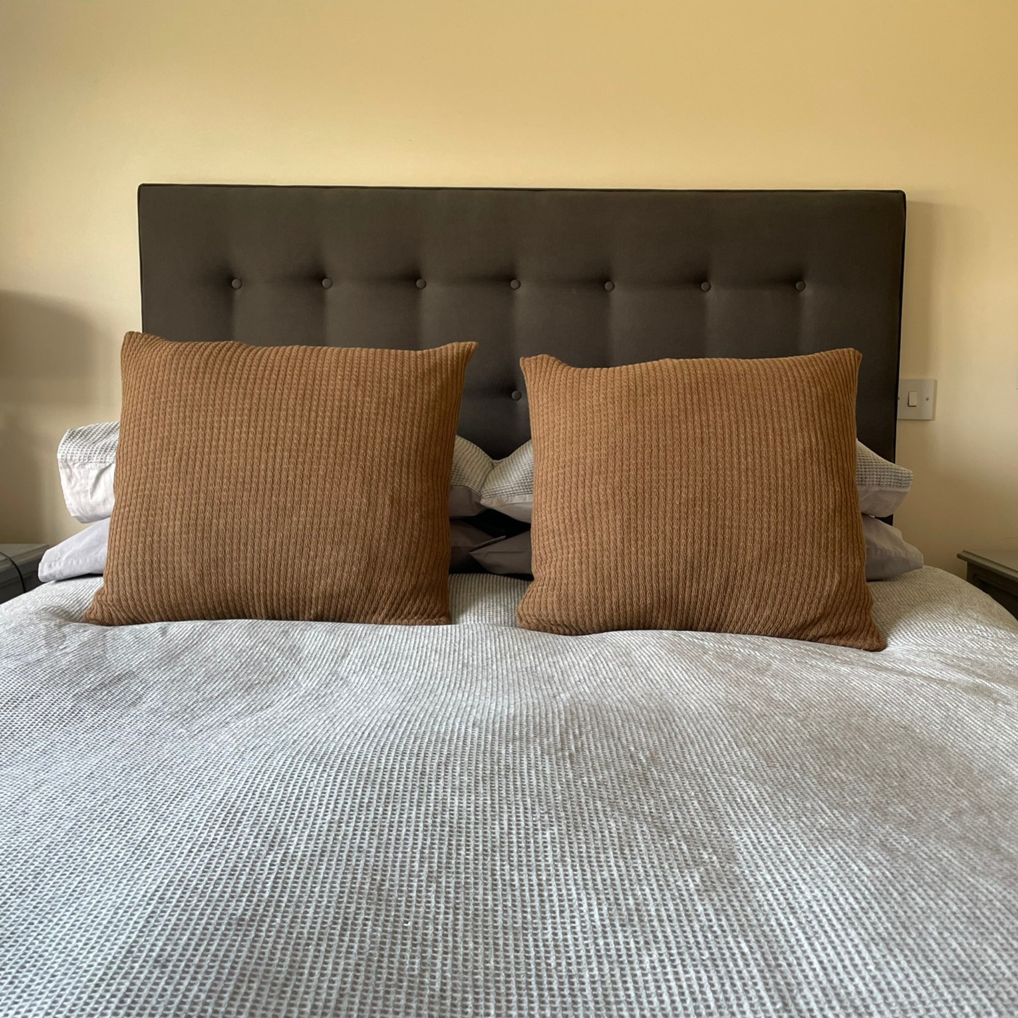 Two large cushions with brown alpaca cushion covers on a bed with grey bedding.