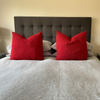 Two large cushions with red alpaca cushion covers on a bed with grey bedding.