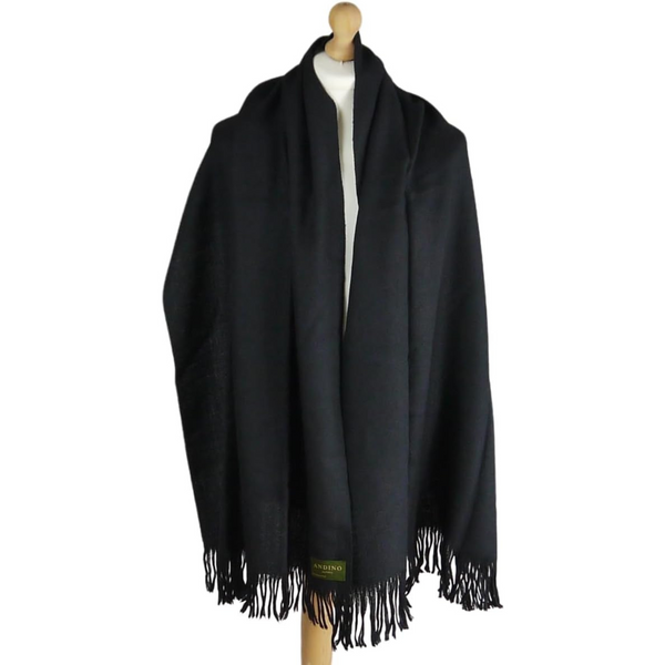 Woman wearing black extra large long alpaca wool scarf with a coat in front of a wall.