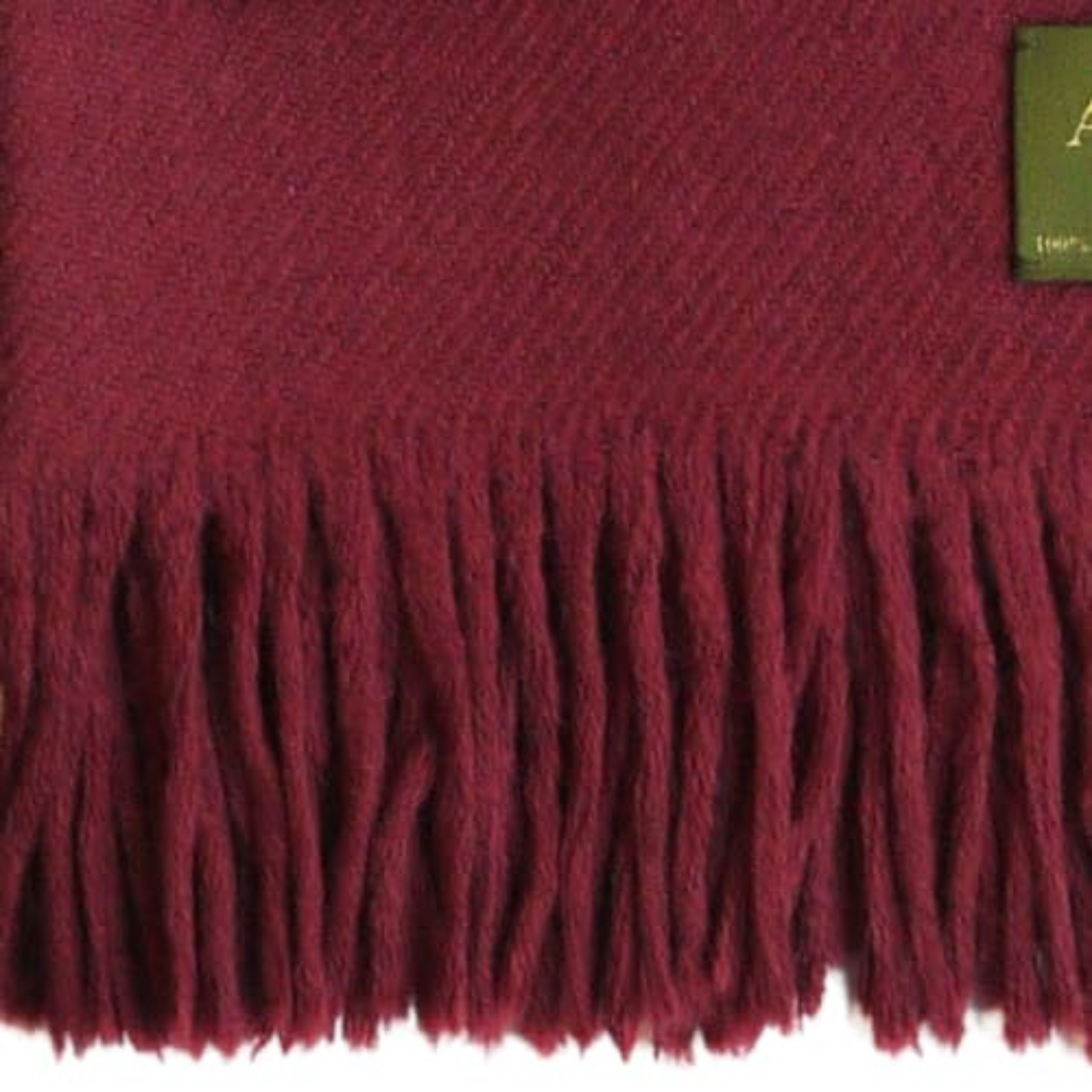 Woman wearing burgundy extra large alpaca shawl in front of a brick wall outdoors.