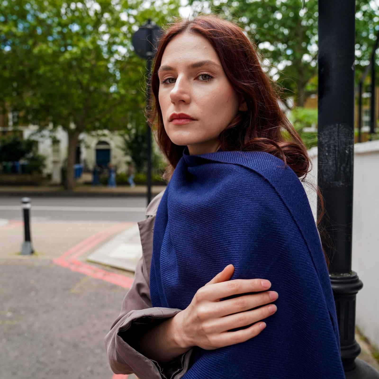 Woman wearing navy blue alpaca scarf shawl extra large & long in a city with streets and trees.