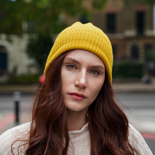 Young man wearing Olive green alpaca beanie hat outdoors in front of a brick wall.