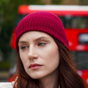 Young woman wearing Burgundy alpaca beanie hat in an outdoor setting in a city with a bus.
