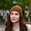 Young woman wearing brown alpaca beanie hat in an outdoor setting in a city.