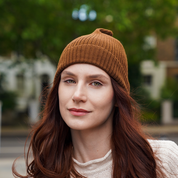 Young woman wearing brown alpaca beanie hat in an outdoor setting in a city.