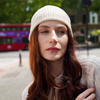 Young woman wearing cream alpaca beanie hat in an outdoor setting in a city with a bus.