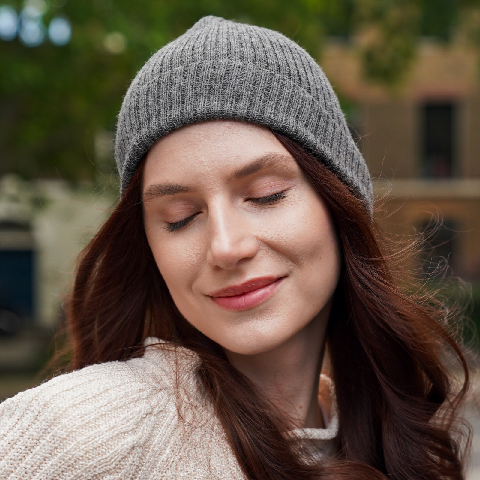 Young woman wearing light grey alpaca beanie hat in an outdoor setting in a city.
