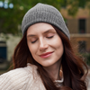 Young woman wearing light grey alpaca beanie hat in an outdoor setting in a city.