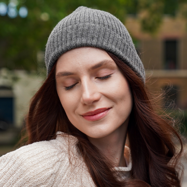 Young woman wearing light grey alpaca beanie hat in an outdoor setting in a city.