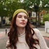 Young woman wearing mustard alpaca beanie hat in an outdoor setting in a city.