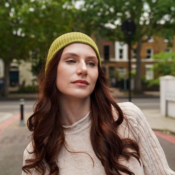 Young woman wearing mustard alpaca beanie hat in an outdoor setting in a city.