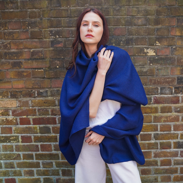 Young woman wearing alpaca blanket as a throw outside in front of brick wall.